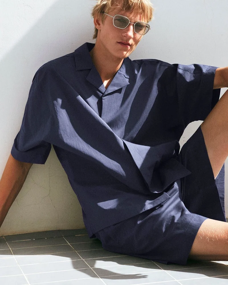 Pierrick Grégoire wearing a navy camp-collar shirt and matching shorts with sunglasses for COS Summer 2026