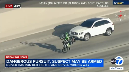 Motorcyclist rides alongside a fleeing Mercedes-Benz during a police pursuit on the 110 Freeway in Los Angeles