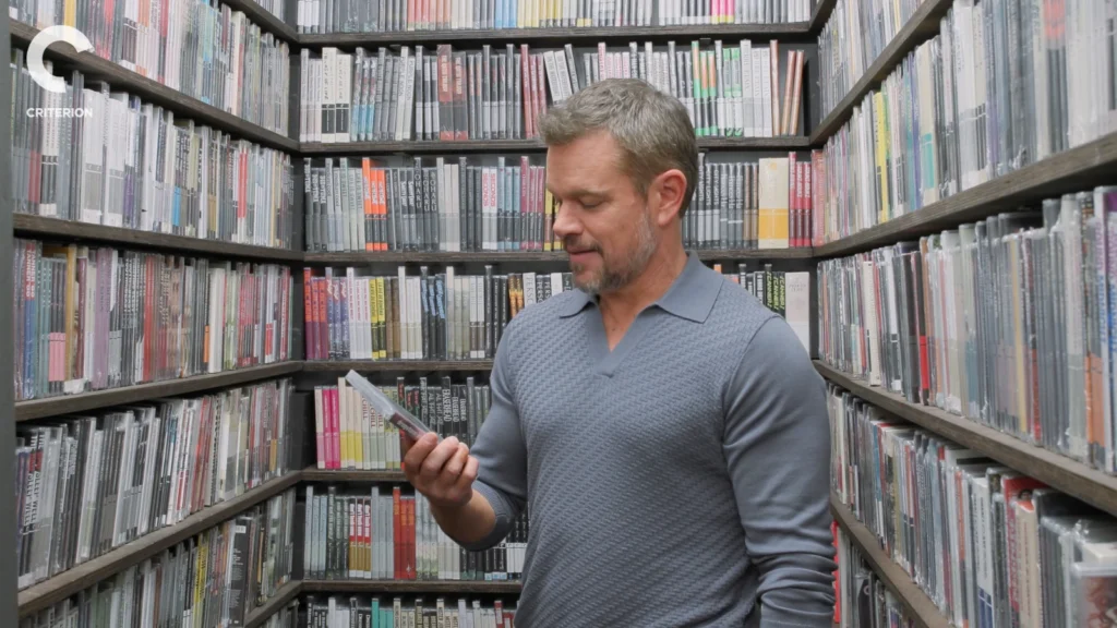 Matt Damon smiles while browsing the Criterion Closet shelves