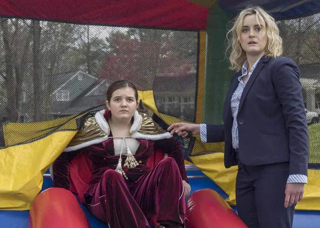 Bryn Vale in a red velvet costume seated beside Taylor Schilling in a bounce house scene from Family