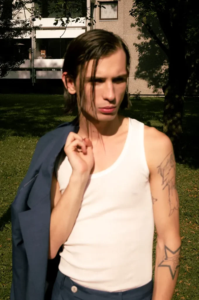 Anton Kügler in a white tank top with a dark suit jacket draped over one shoulder