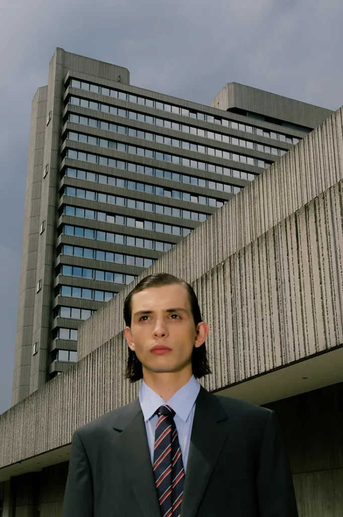 Anton Kügler in a dark suit and striped tie beneath an angular concrete building