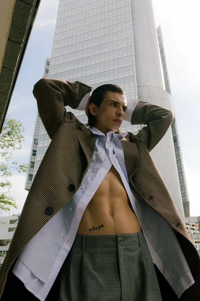 Anton Kügler posing in layered tailoring beneath a glass high-rise
