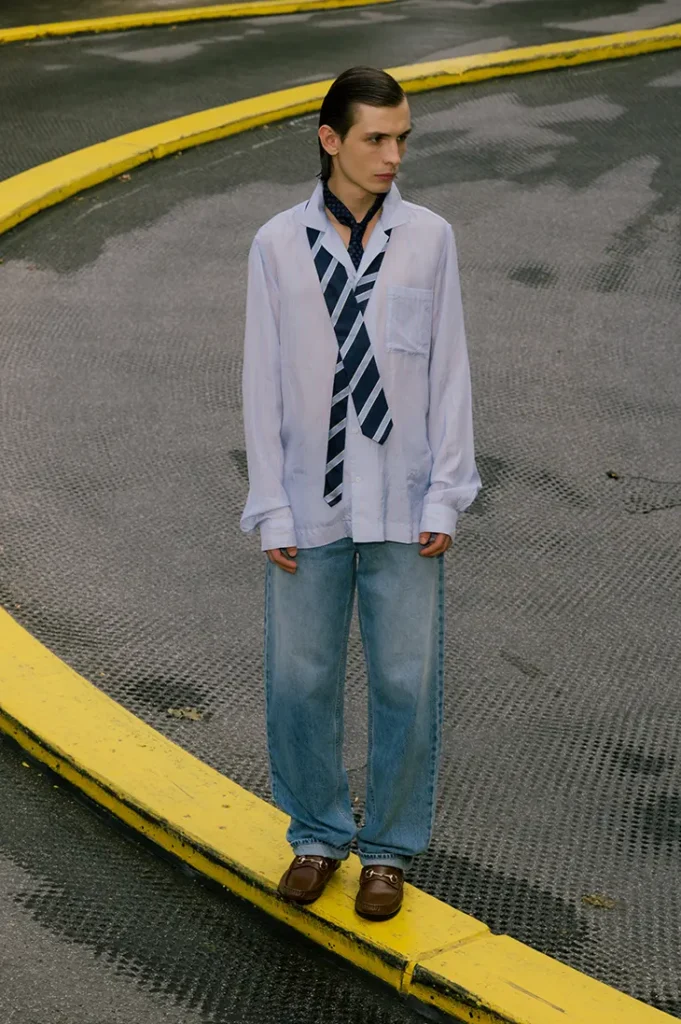 Anton Kügler standing on a yellow curb in a layered shirt, striped tie and jeans