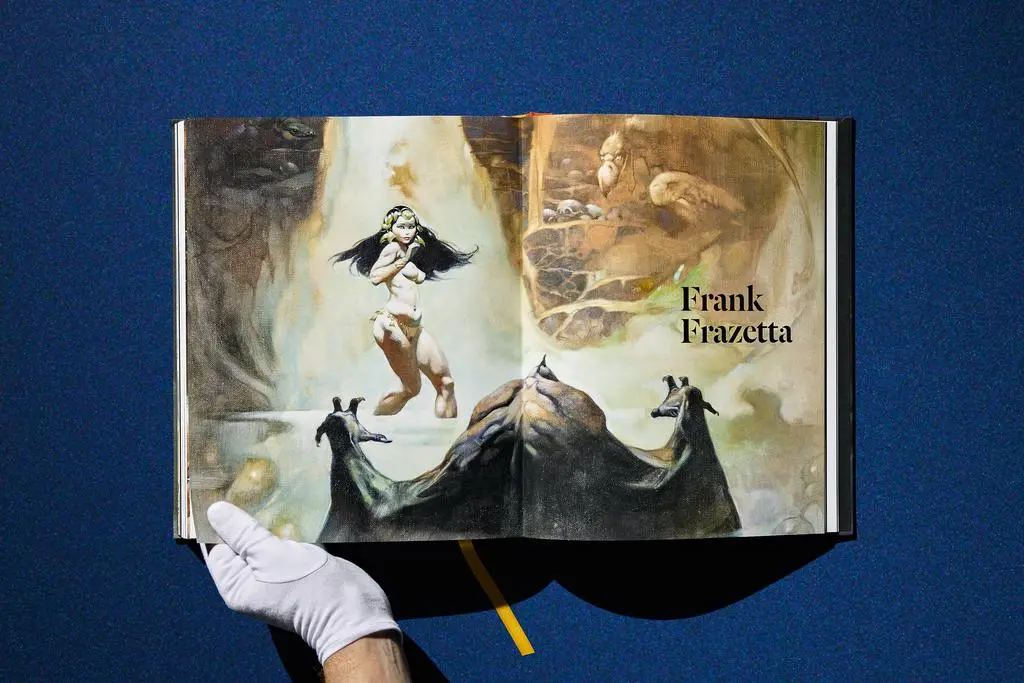 Gloved hands hold open the Lucas Museum of Narrative Art book to a Frank Frazetta spread.