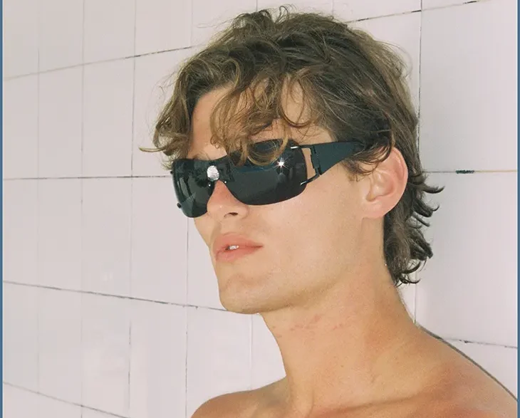 Shirtless model wearing black sunglasses against a pale tiled wall in the Nothing But Summer editorial