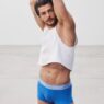 Sam Salter wearing a white cropped tank and blue Calvin Klein trunks with his arms raised