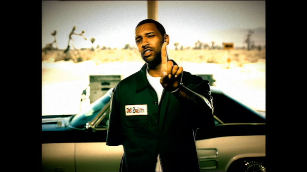 Joe Budden stands beside a car in a scene from the “Whatever U Want” music video.
