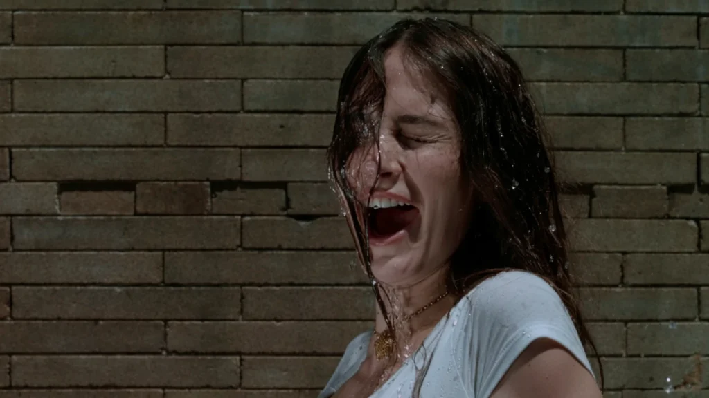 Wet-haired INJI singing in front of a brick wall in the I WANNA FEEL IT ALL music video