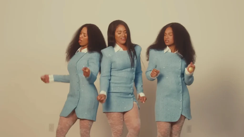 Three women in matching light blue suits pose against a beige backdrop.