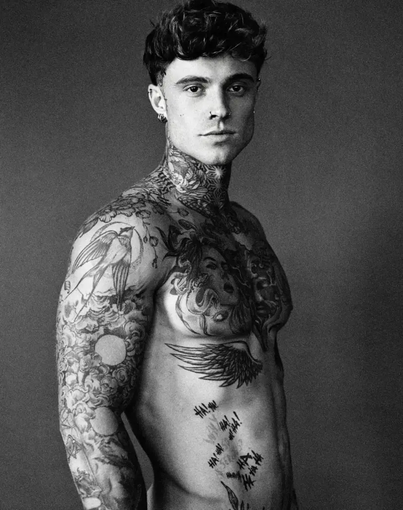 Black-and-white portrait of Samuel Dohmen facing the camera, with tattoos across his neck, chest and arms