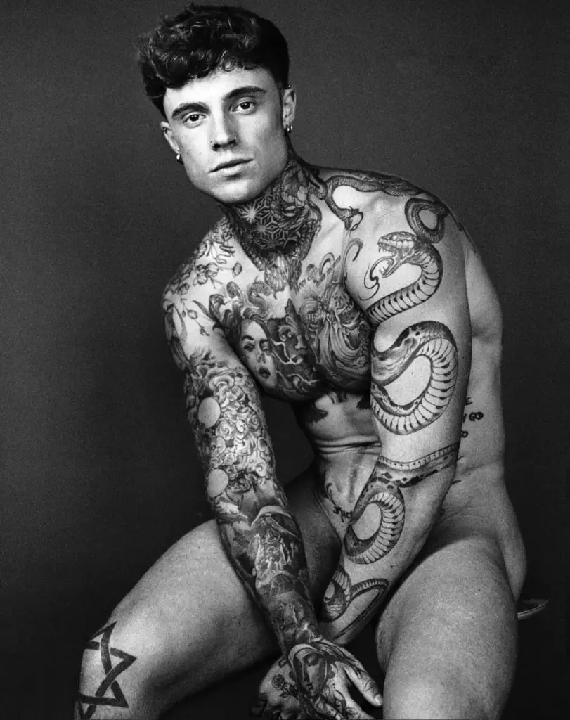 Samuel Dohmen leaning forward in a black-and-white portrait, with tattoos covering his arms and torso