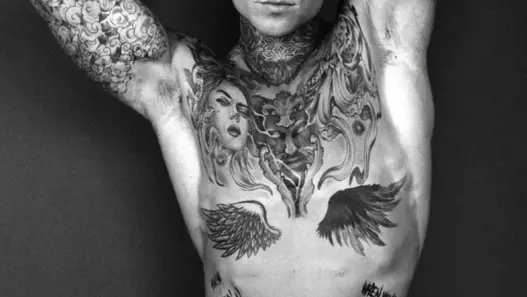 Black-and-white portrait of tattooed model Samuel Dohmen posing with both arms raised above his head, photographed by Richard Kranzin