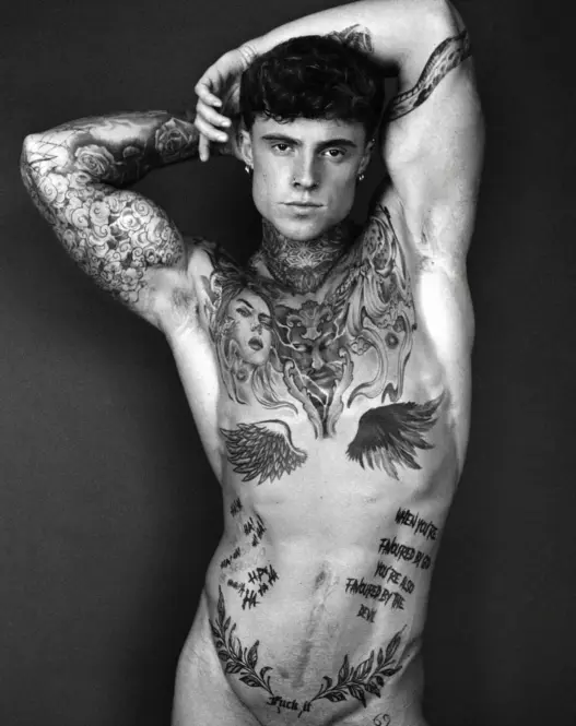 Black-and-white portrait of tattooed model Samuel Dohmen posing with both arms raised above his head, photographed by Richard Kranzin