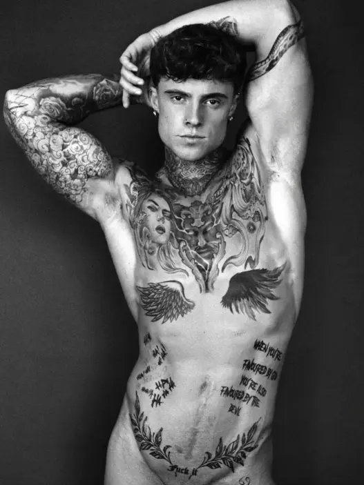 Black-and-white portrait of tattooed model Samuel Dohmen posing with both arms raised above his head, photographed by Richard Kranzin