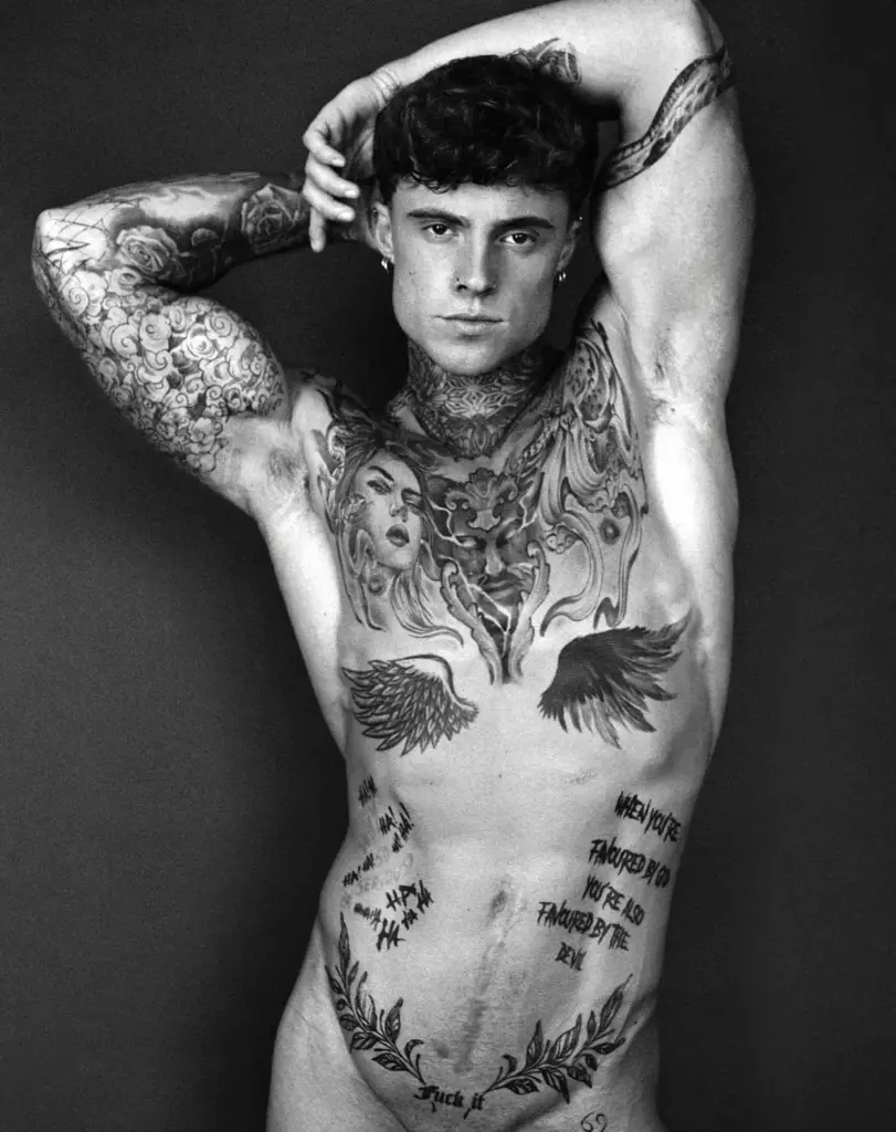 Black-and-white portrait of Samuel Dohmen posing with both arms raised above his head, showing his tattoos