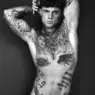 Black-and-white portrait of tattooed model Samuel Dohmen posing with both arms raised above his head, photographed by Richard Kranzin