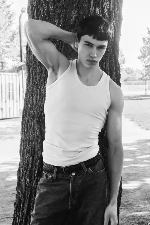 Model Elliot Gareau wearing a white tank top and dark jeans while leaning against a large tree in a black-and-white photograph by Gui Keim for MMSCENE.
