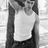 Model Elliot Gareau wearing a white tank top and dark jeans while leaning against a large tree in a black-and-white photograph by Gui Keim for MMSCENE.