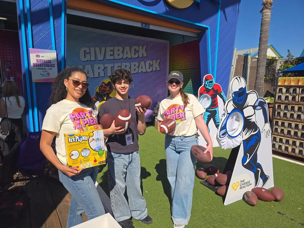 Isaac Ordonez posing with two volunteers holding footballs at Giveback Quarterback