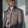 Model David Trulik wearing glasses, a textured gray blazer and layered scarf against a weathered wall in John Varvatos' Fall/Winter 2026 Wonderland campaign, photographed by Cara Johnson.