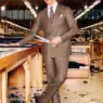 Model Atila Escolano Sanchez wearing a long beige Kiton coat in a tailoring workshop for the Fall/Winter 2026 campaign photographed by Tony Kelly.