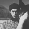 Model Just Verhoeff wearing a dark knit beanie and shearling-lined winter coat beside a horse for Loro Piana's Holiday 2026 campaign.