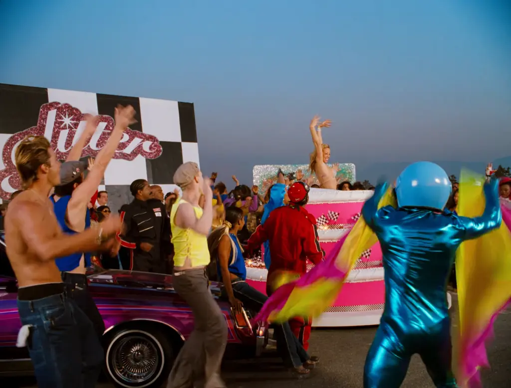 Racetrack crowd and costumed performers in the restored Loverboy Remix music video