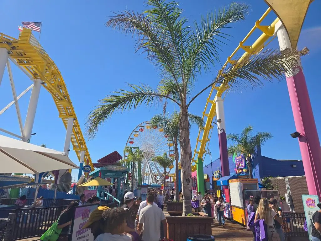 Santa Monica Pier boardwalk with Pacific Park Ferris wheel, roller coaster and palm trees