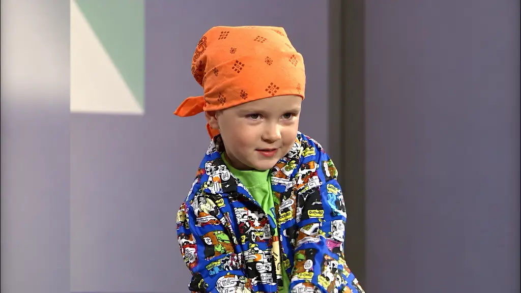 Child model wearing a patterned jacket and orange bandana-style hat during Pee-wee fashion show
