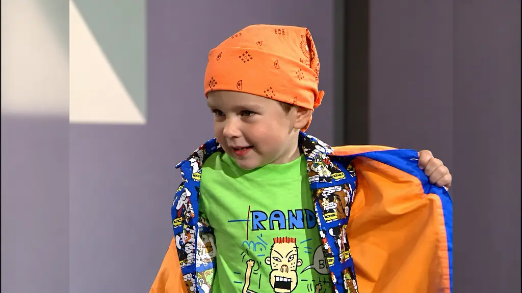 Young model wearing orange cap, bright green shirt and colorful overshirt at the fashion show