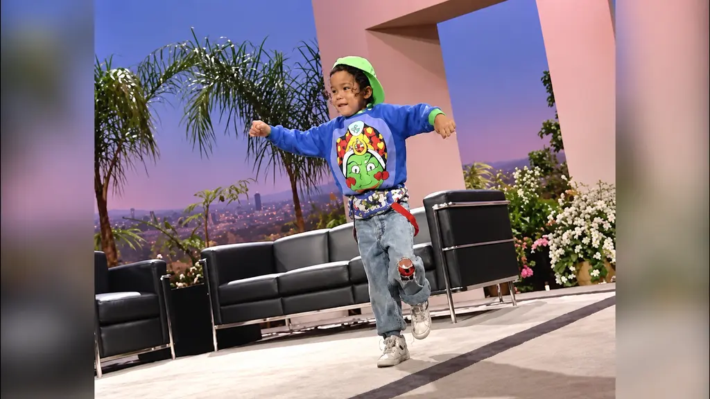 Child model in bright blue sweatshirt and green cap modeling the Pee-wee Herman collection