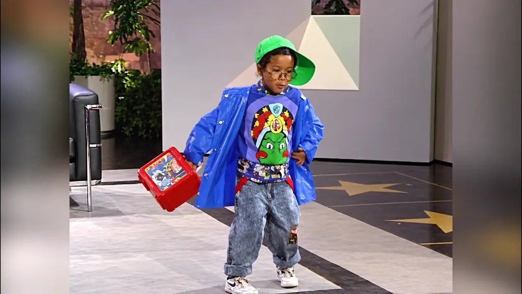 Young model with a green cap and blue Pee-wee top holding a red lunchbox on the set