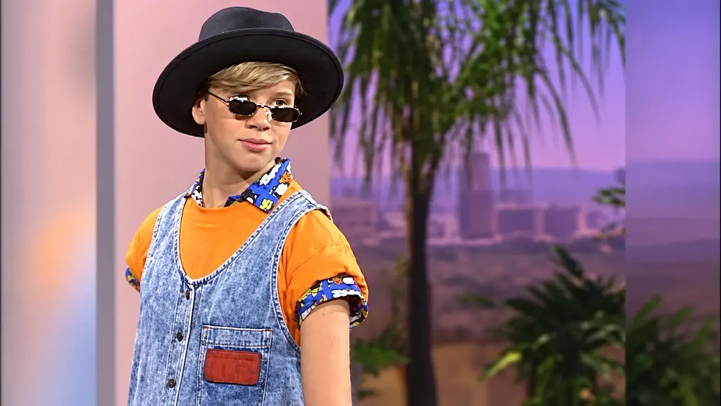 Young model wearing a denim jumper over an orange Pee-wee T-shirt with black hat and sunglasses