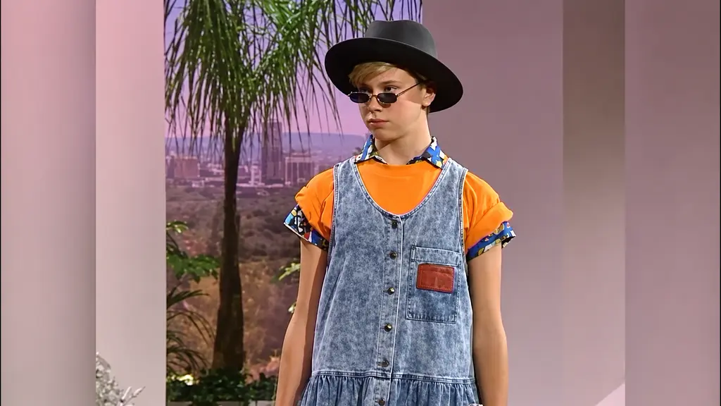 Child model in orange T-shirt, denim jumper dress, hat and sunglasses at the Pee-wee Herman fashion show