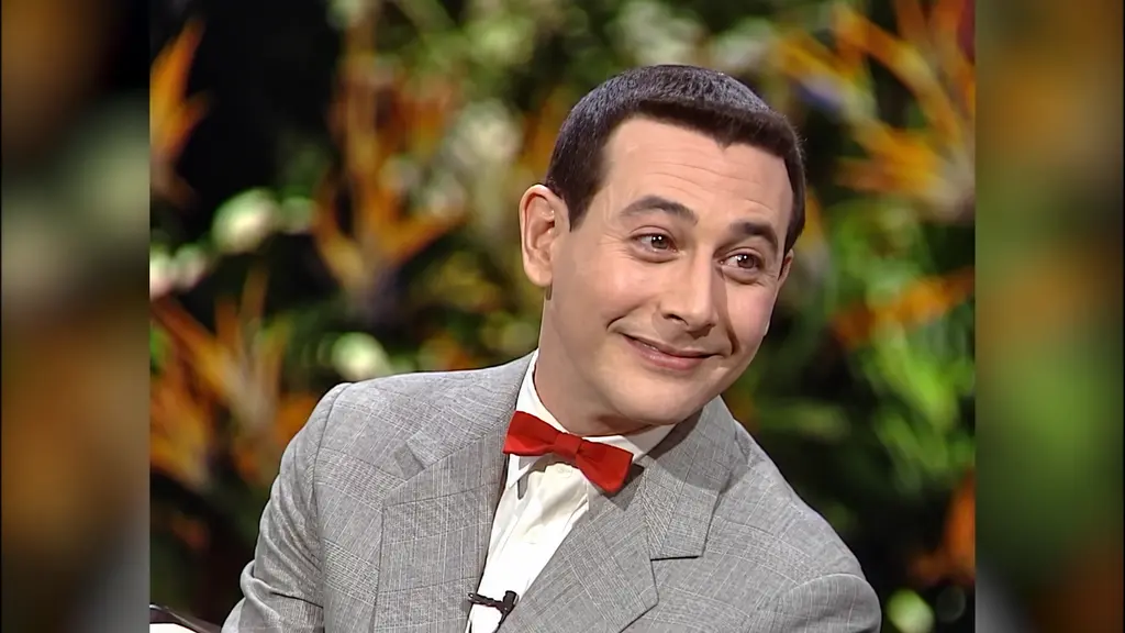 Pee-wee Herman reacting playfully in gray suit and red bow tie during Joan Rivers interview