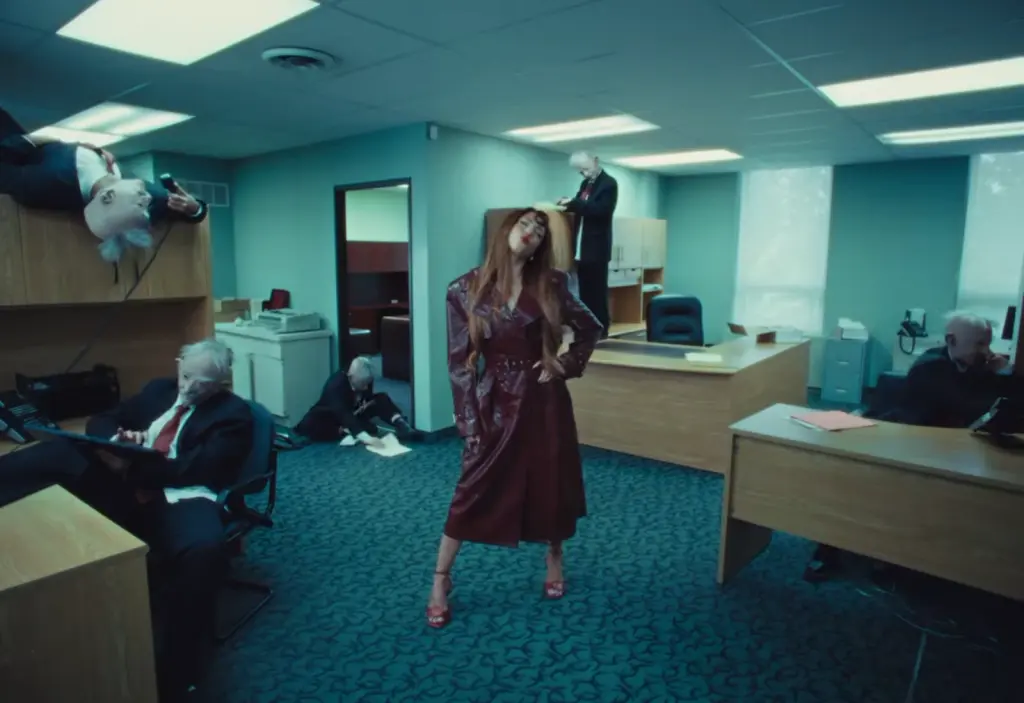 Wide office scene showing Rêve in a burgundy outfit as executives move around the room