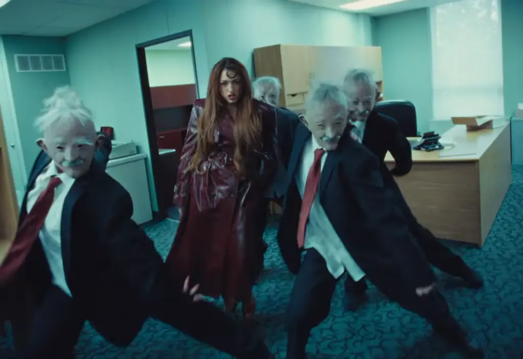 Rêve in a burgundy outfit flanked by two gray-haired suited men in Church of Sound