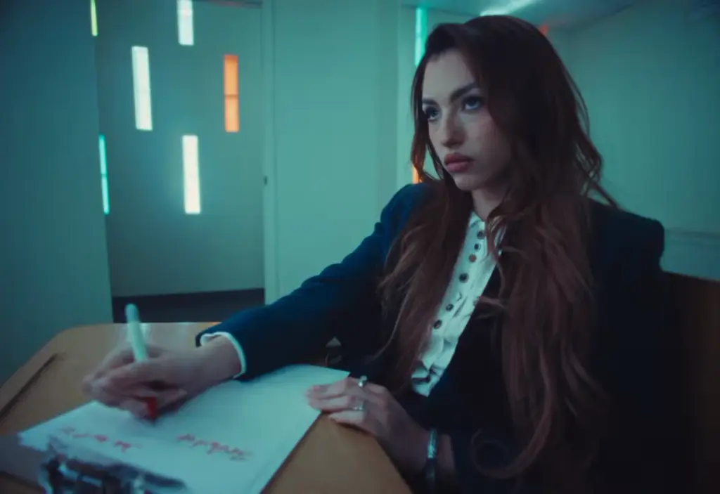 Rêve seated at a desk with pen and open notebook during the Church of Sound video