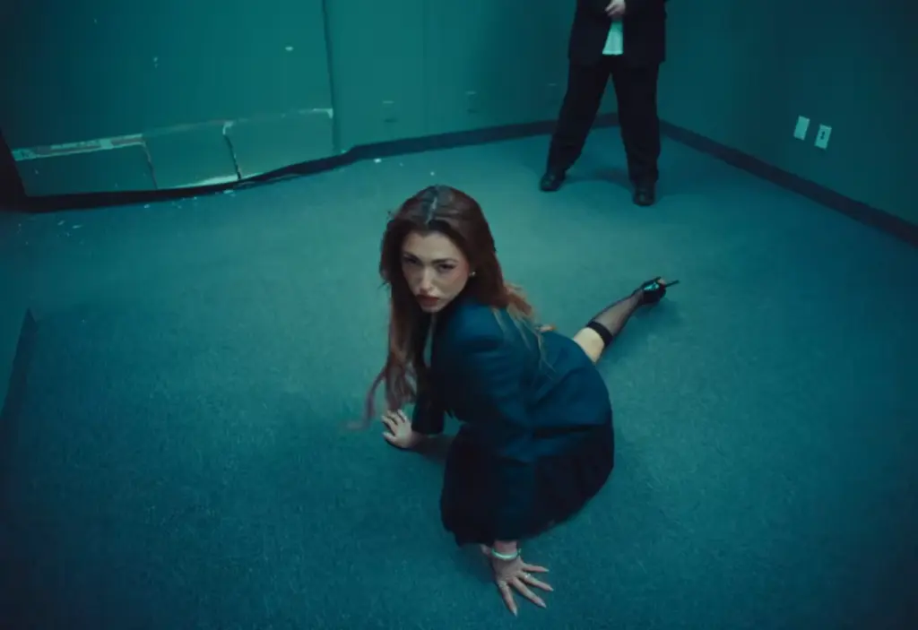 Rêve crouching on an office carpet with a suited man behind her in Church of Sound