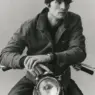 Male model wearing a dark workwear jacket and black trousers, posing beside a sculptural lamp in a black-and-white image from Taylor Stitch's North By Northwest Winter 2026 collection.