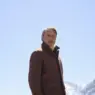 Mads Mikkelsen wearing a brown Zegna Falcon jacket over a beige turtleneck against snow-covered mountains for the Fall/Winter 2026 campaign.