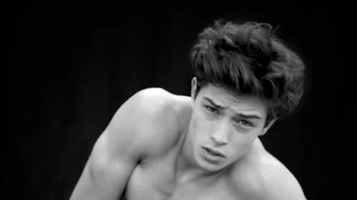 Francisco Lachowski kneels in jeans, shirtless, against a dark background in a black-and-white fashion portrait.