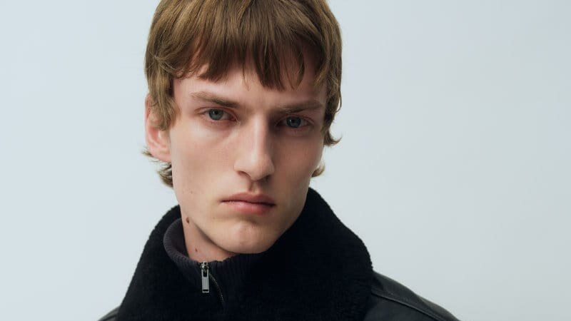 Model wearing a black leather jacket with a plush high collar and front button closure.