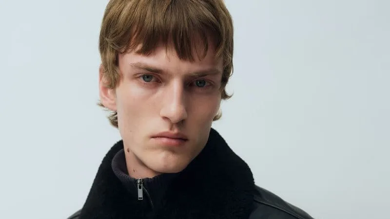 Model wearing a black leather jacket with a plush high collar and front button closure.