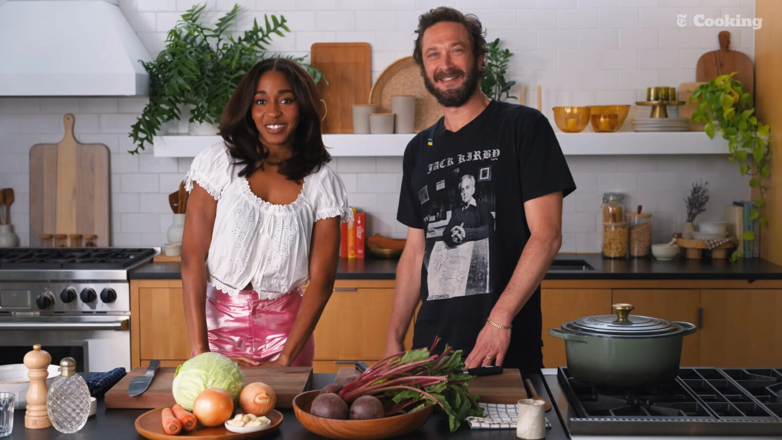 Ayo Edebiri and Ebon Moss-Bachrach stand together in a kitchen beside vegetables, beets and a covered pot.