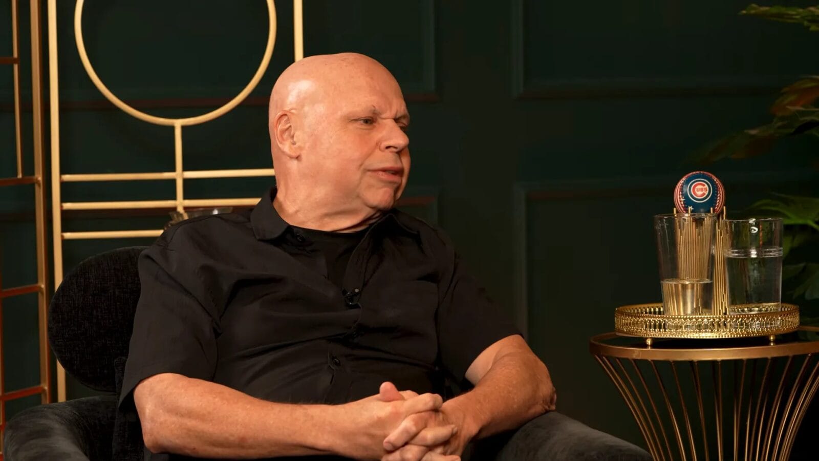 Billy Corgan sits in a dark studio setting, wearing a black shirt with his hands clasped.
