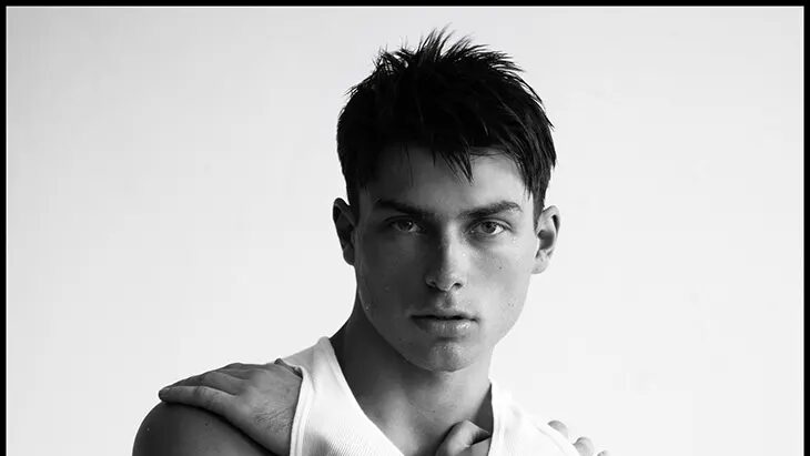 Max Luc faces the camera in a black-and-white portrait while crossing his arms over a white tank top.