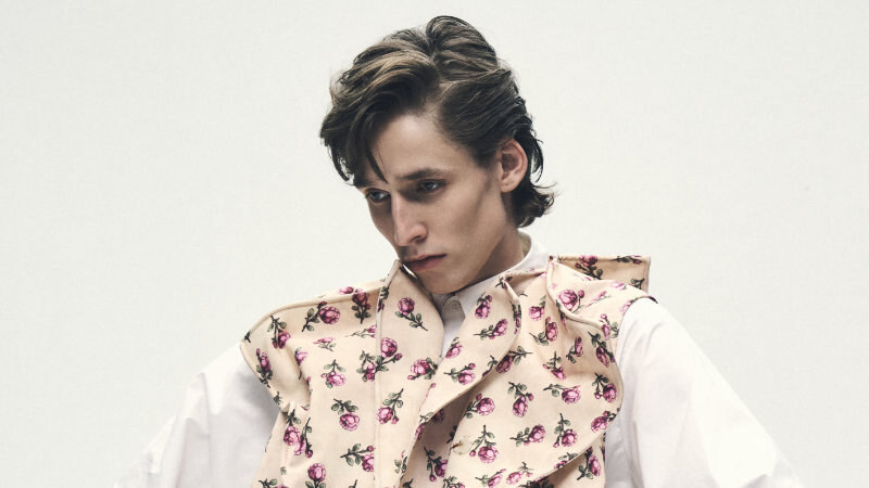 Model wearing a pink floral tailored vest and matching trousers over a voluminous white shirt, posed against a pale background.