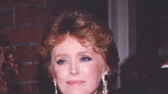 Rue McClanahan holds an Emmy Award while wearing a black outfit and dangling earrings.